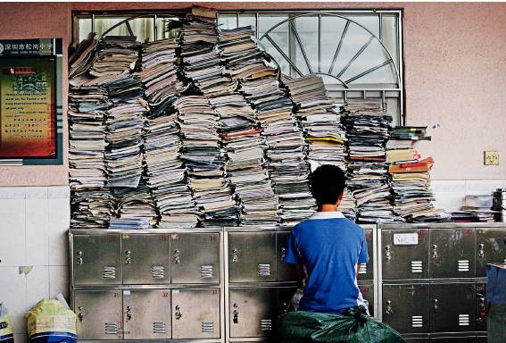 一名高三学生坐在由复习资料砌成的“书墙”前翻阅高考模拟试卷。图/视觉中国